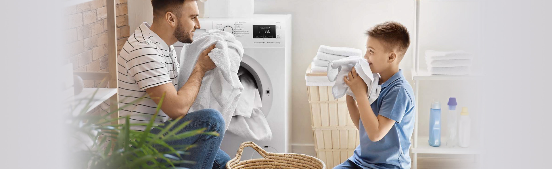 Mann und Kind riechen an Handtüchern vor einer Waschmaschine
