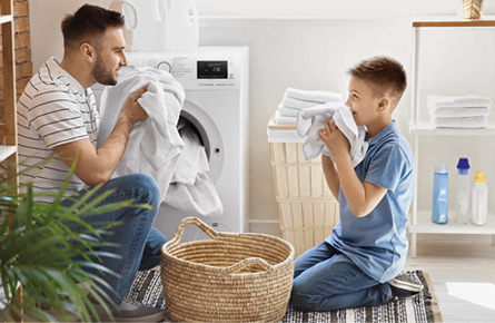 Mann und Kind riechen an Handtüchern vor einer Waschmaschine
