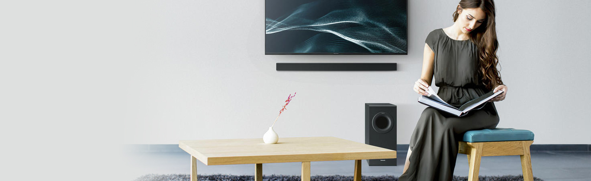 Frau ließt ein Buch vor einem Fernseher mit Soundbar und Subwoofer