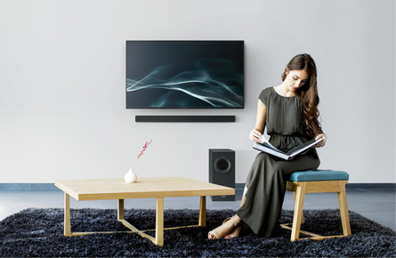 Frau ließt ein Buch vor einem Fernseher mit Soundbar und Subwoofer