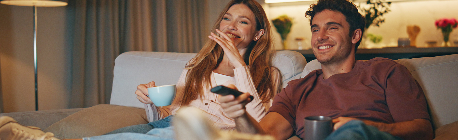 Ein Mann und eine Frau sitzen auf einer Coach und haben eine Fernbedienung in der Hand
