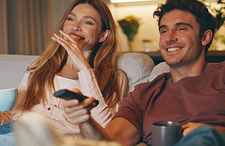 Ein Mann und eine Frau sitzen auf einer Coach und haben eine Fernbedienung in der Hand