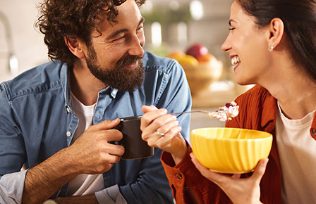 Ein Mann und eine Frau sitzen in der Küche und essen Müsli und trinken Kaffee