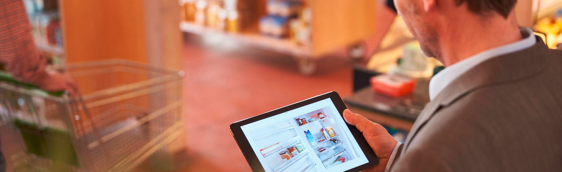 Mann schaut auf ein Bild eines geöffneten Kühlschranks auf einem Tablet