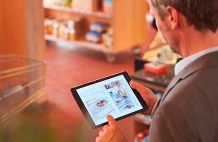 Mann schaut auf ein Bild eines geöffneten Kühlschranks auf einem Tablet