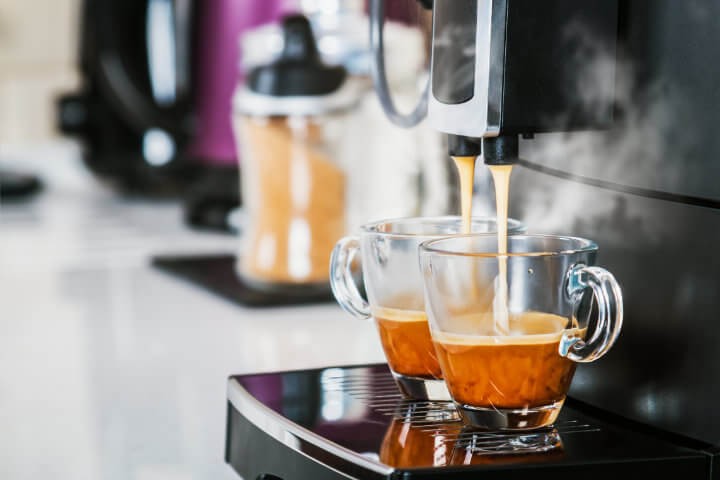 Frisch gebrühter Kaffee läuft aus einer modernen Kaffeemaschine in eine Glastasse